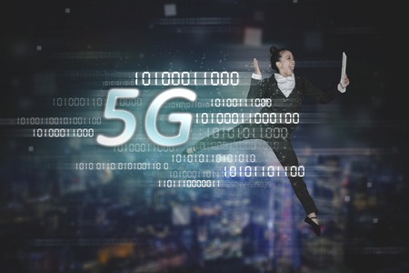 Businesswoman using a digital tablet while dancing with 5G network symbol and binary code