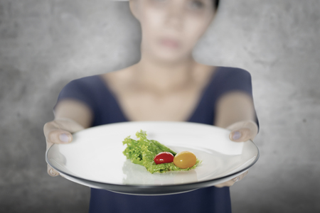 Blurred background of young woman showing a plate of small portion salad. Diet conceptの写真素材