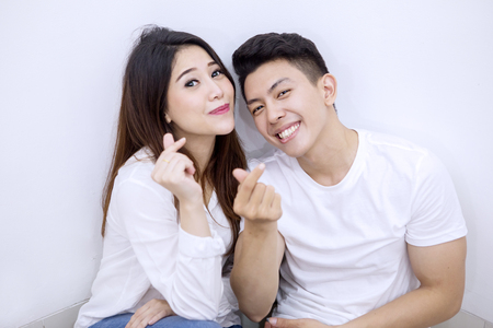 Young couple smiling at the camera while gesturing money with their hands, isolated on white backgroundの写真素材
