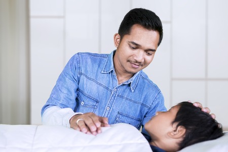 Close up of an Asian father giving support for his sick son while lying on the hospital bed
