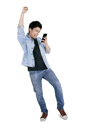 Full length of a young happy man holding a mobile phone while celebrating his success in the studio