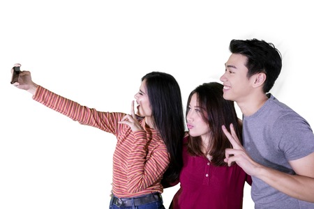 Young woman using a smartphone to take a selfie photo with her friends, isolated on white background