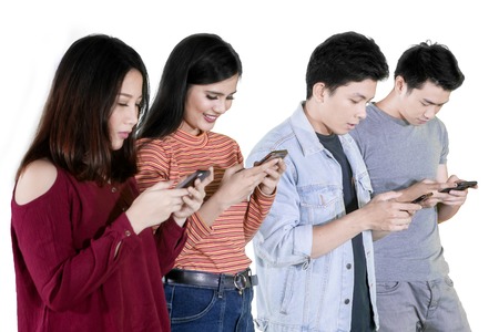 Group of young Asian people looking down at mobile phone and standing in the studio, isolated on...