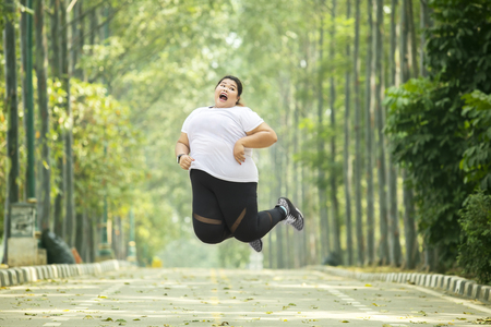 Picture of an excited fat woman leaping on the road while wearing sportswearの写真素材