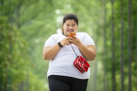 Picture of overweight woman looks happy while using a mobile phone in the parkの写真素材