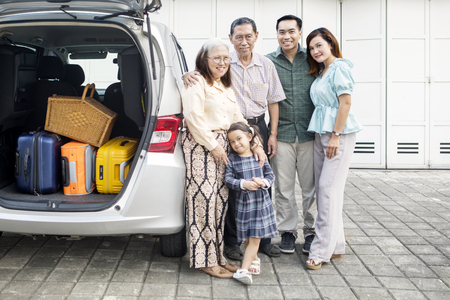 Smiling big family ready to holiday while standing near their car in the house garageの写真素材