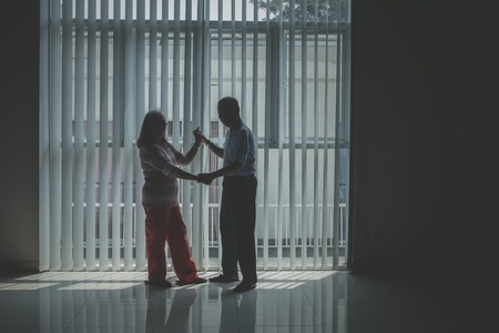 Silhouette of senior couple looking at the camera while dancing near the window. Shot in the dark roomの写真素材