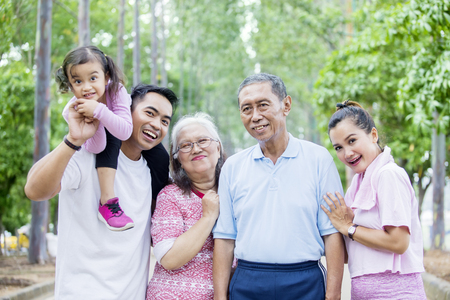 Three generation family smiling together at the camera while standing on the road. Shot at the park