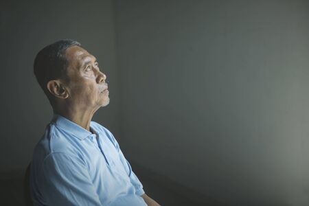 Picture of sad old man daydreaming and sitting alone in the dark room