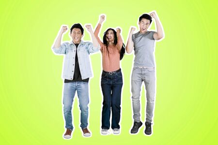Pretty girl lifting hands with her friends while celebrating their success in the studio with green...