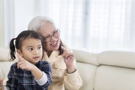 Picture of cheerful old woman watching TV with her grandchild at homeの写真素材