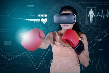 Young woman wearing boxing gloves and VR glasses while exercising with virtual simulation