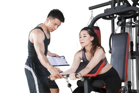 Picture of male trainer guiding his client to train with a machine exercise, isolated on white...
