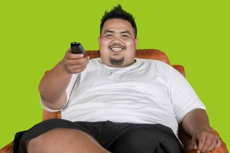 Picture of a happy fat man watching television while sitting in the armchair with green screenの写真素材