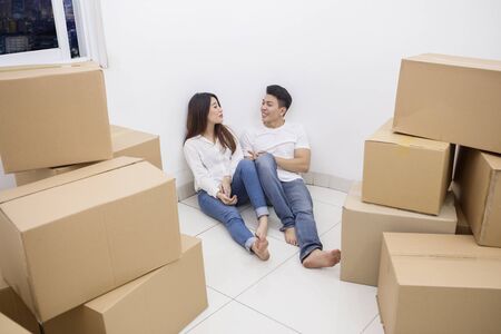 Picture of young couple chatting together while sitting near stacks of cardboard boxes in the new apartmentの写真素材