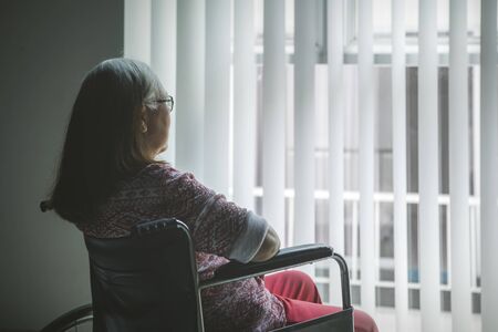 Rear view of a disabled old woman sitting in a wheelchair while looking out the window