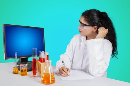 Female researcher working with paper, computer and test tubes on the table with green screen backgroundの写真素材