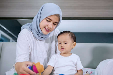 Image of young woman wearing veil while playing with her baby girl in the bedroomの写真素材