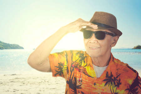 Picture of old man wearing summer clothes and hat while looking far away at sea and standing on the beachの写真素材