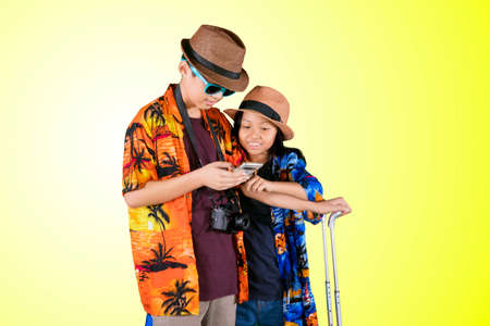 Two child tourists wearing summer clothes while using a mobile phone in the studio