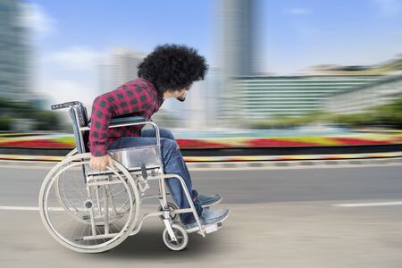 Side view of disabled Afro man sitting on a wheelchair while walking on the road with fast motion blurの写真素材