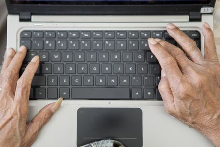 Closeup of senior man hands typing on the laptop computer keyboard at homeの写真素材