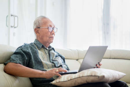 Senior man working with laptop computer while sitting on the sofa in living room at home