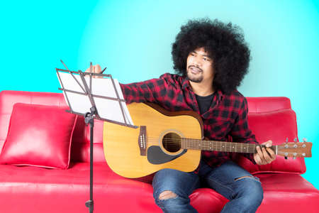Young musician writing a song while playing a guitar and sitting on the couch. Shot in the studio