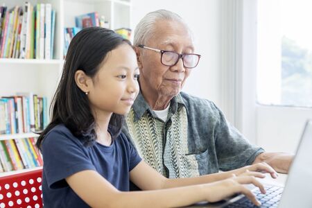 Portrait of elderly man and his granddaughter using a laptop computer on the table at home