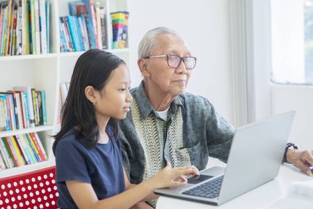 Pretty little girl using a laptop computer with her grandfather in the libraryの写真素材