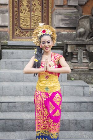 Friendly attractive balinese dancer in traditional costume, smiling at the camera while showing a welcome gesture in the templeの写真素材