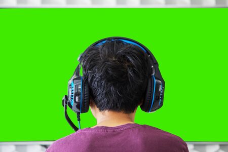 Back view of young preteen boy watching TV while wearing headphone at homeの写真素材