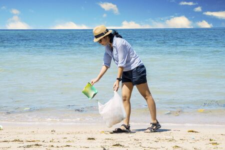 Young woman cleaning beautiful beach by picking plastic wasteの写真素材