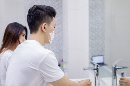 Picture of young man cleaning his razor while standing with his wife in the bathroomの写真素材
