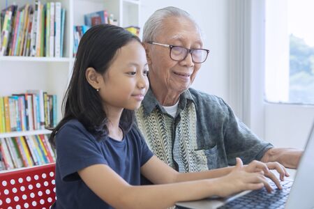 Picture of little girl learning to use a laptop computer with her grandfather in the libraryの写真素材