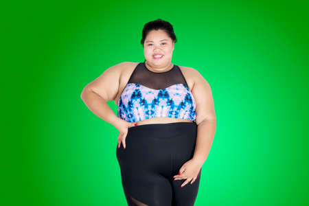 Picture of young obese woman looks confident while wearing sportswear in the studio with green screen backgroundの写真素材