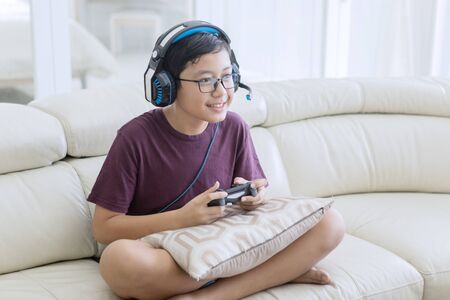 Picture of happy teen boy wearing headphones while playing video games with a joystick at home
