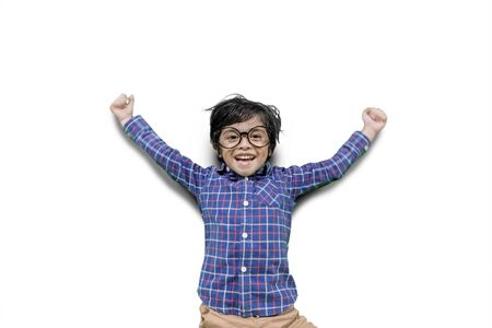 Cheerful little boy jumping and lifting arms in the studio, isolated on white backgroundの写真素材