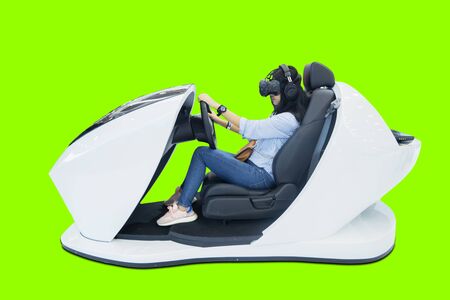 Young woman driving a car simulator while wearing a VR glasses in the studio with green screen...