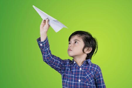 Picture of a cute little boy throwing a paper plane while playing in the studio with green screen backgroundの写真素材