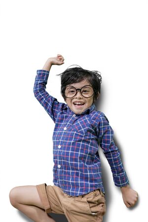 Portrait of a cheerful little boy wearing glasses while jumping in the studio, isolated on white backgroundの写真素材