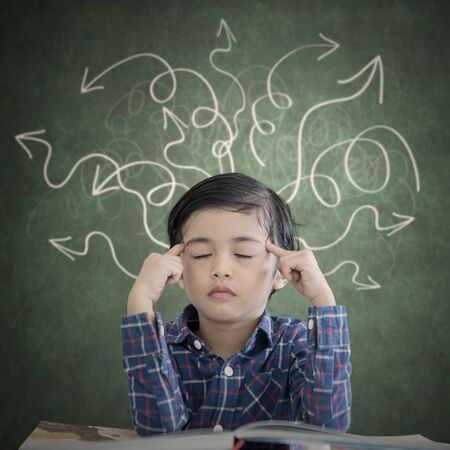 Picture of little boy thinking with eyes closed while sitting with arrow chaotic symbols over his...