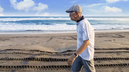 Side view of elderly man walking in the Papuma beach with beautiful seascape backgroundの写真素材