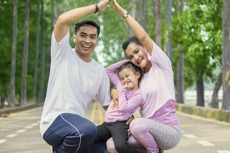 Portrait of cheerful family making house symbol with their hands in the park