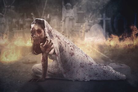 Halloween horror concept. Horrible bride ghost crawling in the burning cemetery