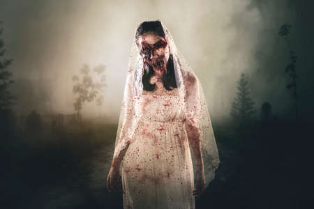 Creepy female ghost wearing bloody bride gown and standing in the cemetery. Halloween horror concept
