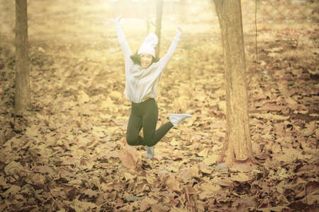 Picture of young man looks happy while jumping in the autumn park with dried autumn foliageの写真素材