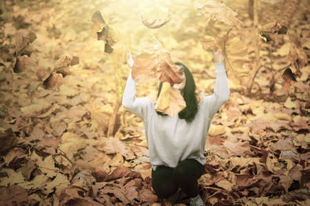 Cheerful young woman enjoying holiday at the autumn park and throwing autumn leaves. Shot outdoorsの写真素材