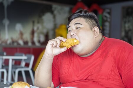 Portrait of obese man enjoying crunchy fried chicken in the restaurant. Unhealthy lifestyle concept.の写真素材