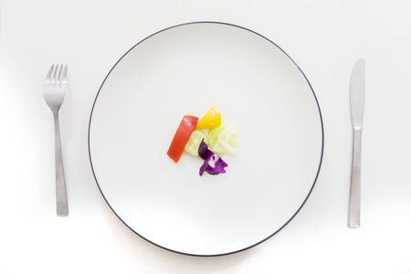 Unhealthy diet concept. Top view of a small portion of vegetable salad serving on the table with fork and knifeの写真素材